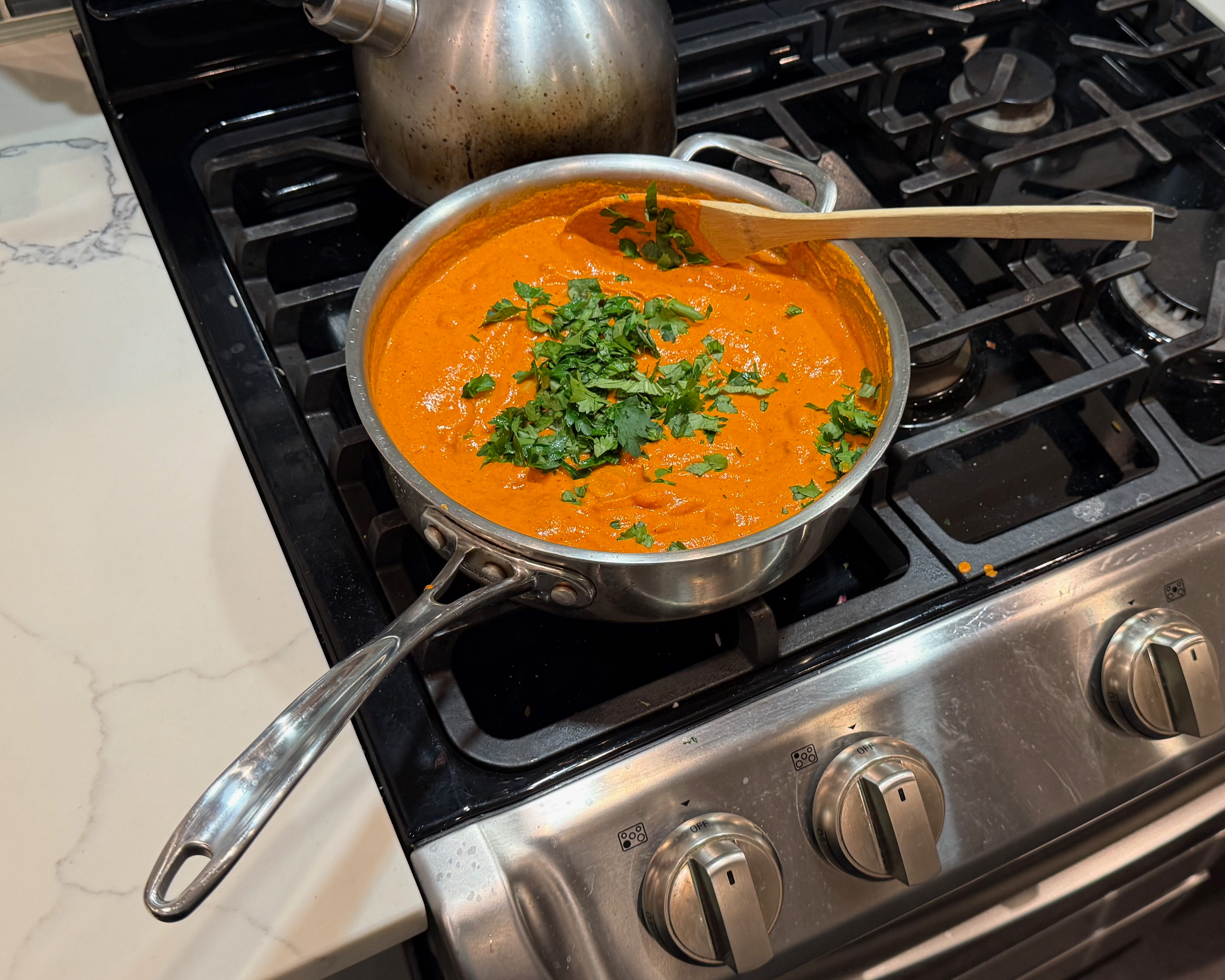 A pan on a stove contains an orange sauce